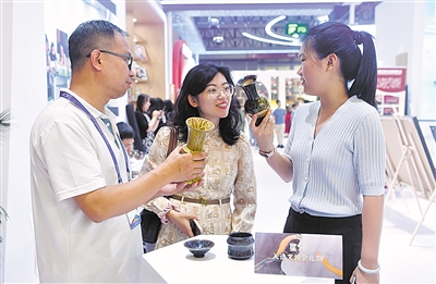 宁夏天天互联文化传媒有限公司负责人（左）向逛展市民介绍黄河古瓷花瓶·星河产品。                本报记者  王晓龙 陈郁 摄